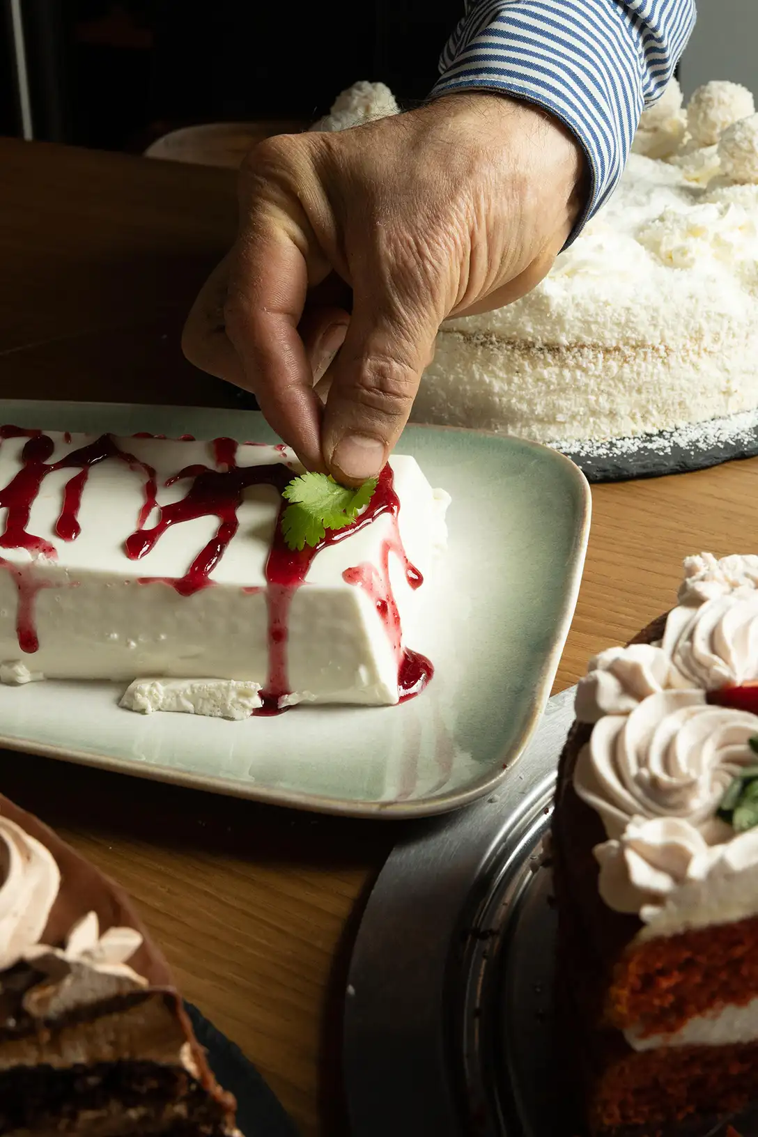 Saverio termina a mano un postre casero con salsa de frutos rojos, con tartas de la casa al fondo